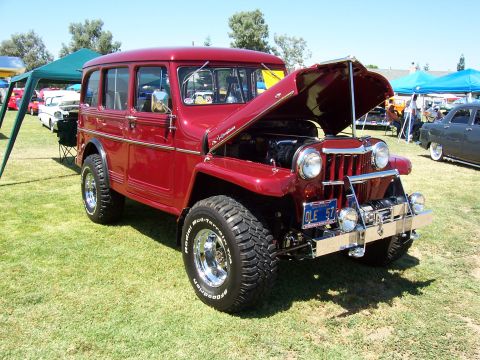 2002 Ford Mustang - Vintage red station wagon SUV parked on grass with hood open, other vehicles and tents in background.
