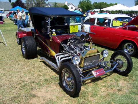 2002 Ford Mustang - A custom hot rod with a large engine and flame decals is displayed at an outdoor event.