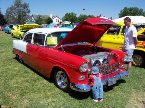 2002 Ford Mustang - A classic red and white Chevrolet sedan, likely a 1955 model, is displayed with its hood open, attracting the attention of a small child.