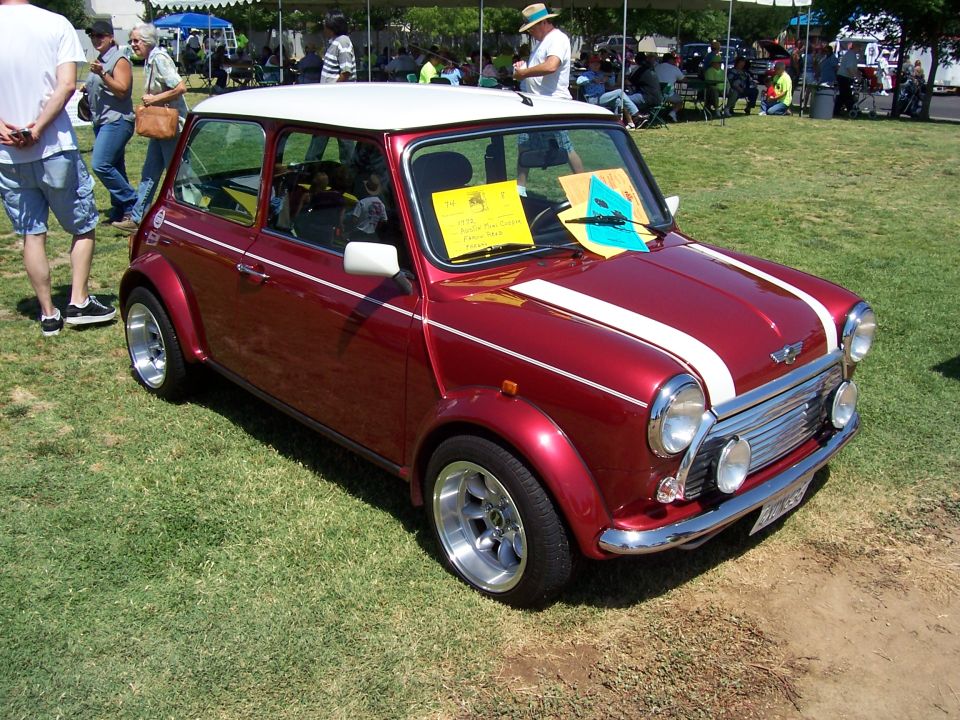 Red Mini Cooper with white roof, white racing stripes on hood, and chrome accents parked on grass