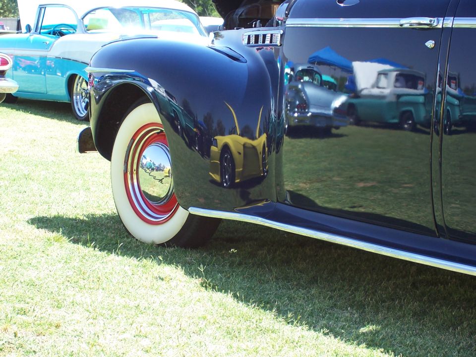 Dark vintage car side view, showing whitewall tire with red and chrome trim, and reflections of other vehicles