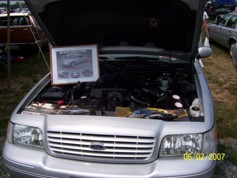 2003 Ford Crown Victoria - The engine bay of a silver 2003 Ford Crown Victoria is displayed with a framed picture and a model car.