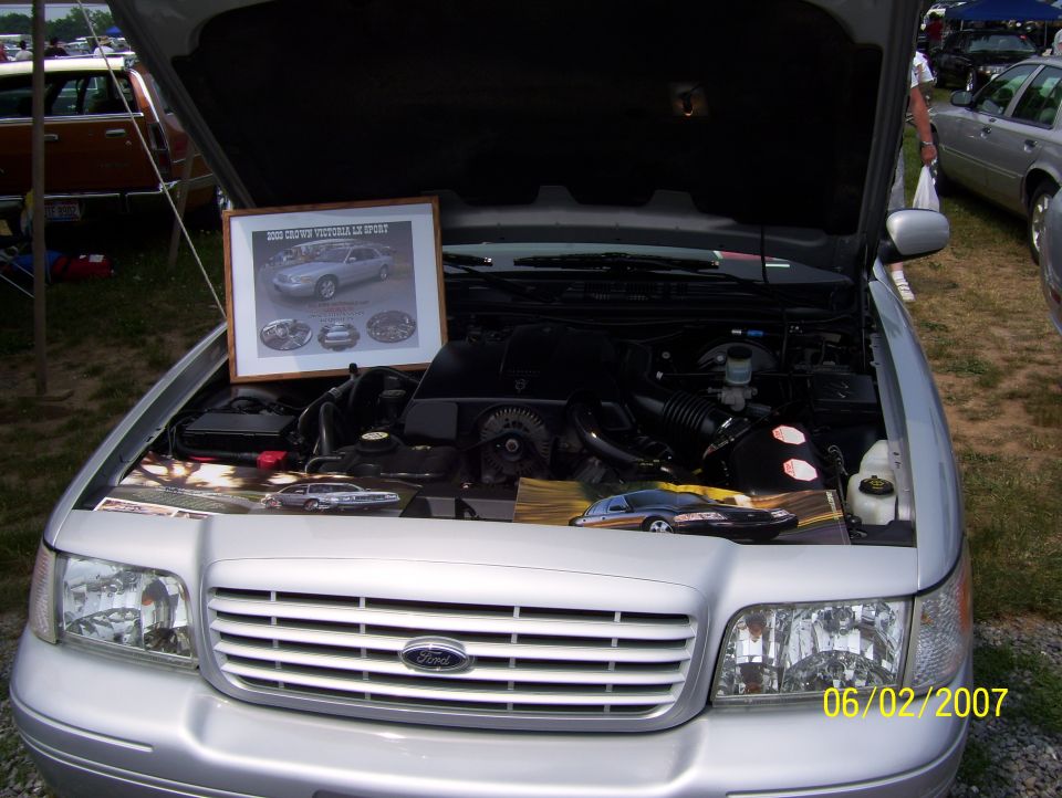 Silver 2003 Ford Crown Victoria engine bay, hood open, with a framed display and model car