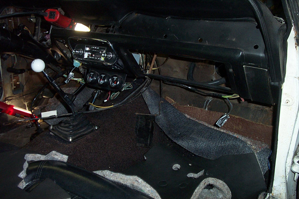 Interior view of a classic car's dashboard and floor, showing a manual shifter and radio