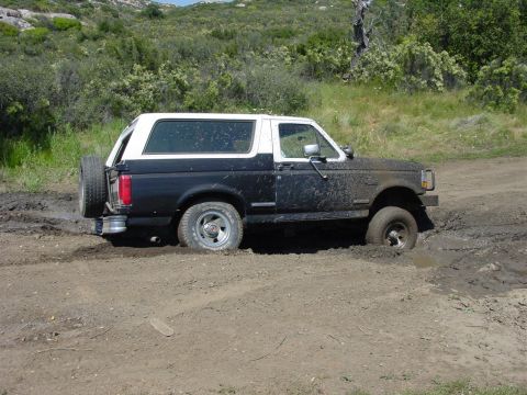 1994 Ford Bronco - Ford Bronco stuck in mud on a dirt road with green hills in the background.