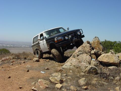 1994 Ford Bronco - A two-tone Ford Bronco navigates a rocky incline under a clear blue sky.