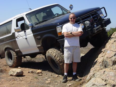 1994 Ford Bronco - A man stands next to a modified Ford Bronco navigating a rocky incline.