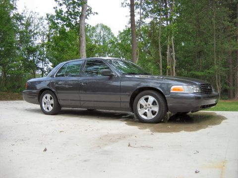 1985 Ford LTD Crown Victoria - A dark gray sedan is parked on a concrete pad with trees visible behind it.