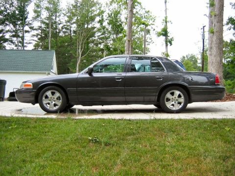 1985 Ford LTD Crown Victoria - A side profile of a dark gray Ford Crown Victoria is shown parked on a driveway with a grassy lawn in the foreground.