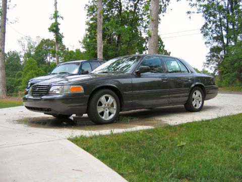 1985 Ford LTD Crown Victoria - A dark gray sedan is parked on a driveway next to an SUV. The sedan appears to be a 1998 Ford Crown Victoria.