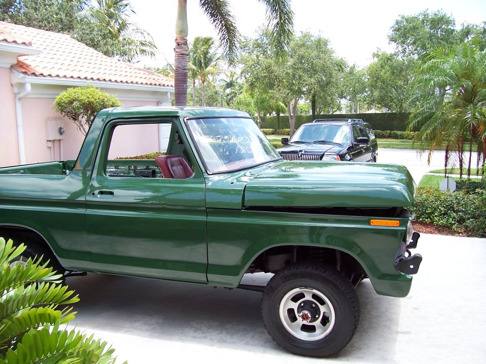 Green 1978 Ford Bronco parked in driveway with a black SUV behind it