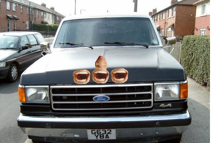 Front view of a Ford truck with a nose and three mouths stuck on the hood. License plate G632 YBA