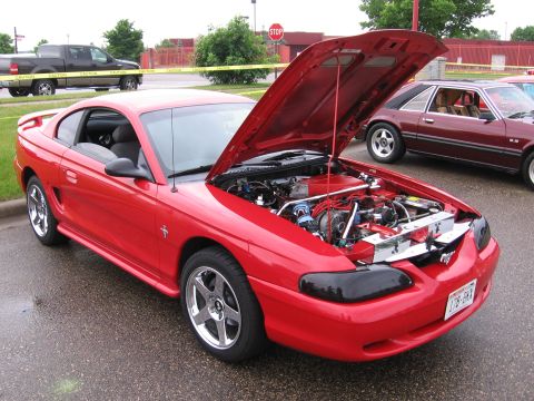 1989 Ford Mustang - Red coupe with hood open, revealing the engine bay. A second car is visible in the background.