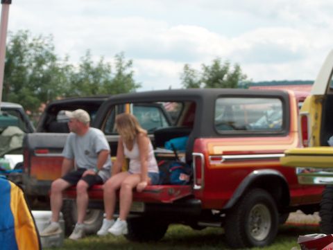 1978 Ford Bronco - Two people relax on the tailgate of a red 1978 Ford Bronco at an outdoor gathering.