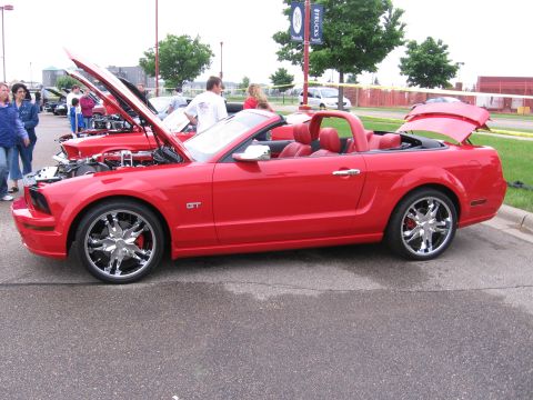 1989 Ford Mustang - A red convertible Mustang GT is displayed with its hood and trunk open, alongside other vehicles.