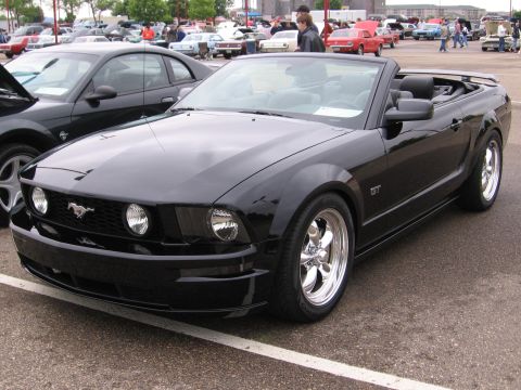 1989 Ford Mustang - Black convertible Ford Mustang parked at an outdoor car show with other vehicles in the background.