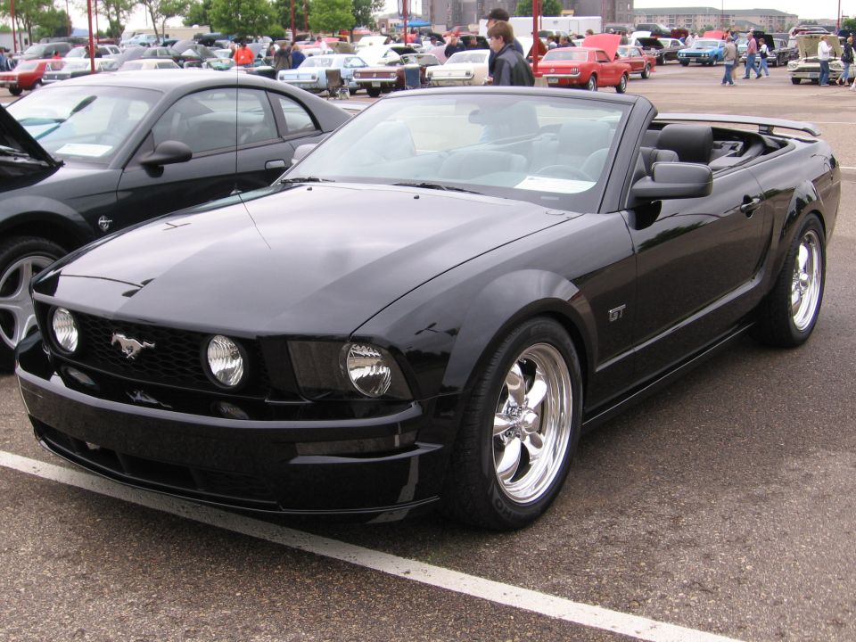 Black convertible Ford Mustang with chrome wheels parked at an outdoor car show