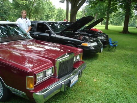 1992 Ford Crown Victoria - A trio of black Ford Crown Victorias are displayed with their hoods open at an outdoor event.
