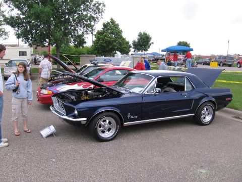1989 Ford Mustang - A dark blue classic car with flame decals is displayed at a car show with its hood open.