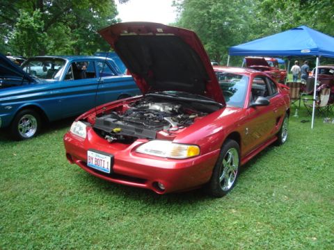 1992 Ford Crown Victoria - A red Ford Mustang is displayed with its hood open at an outdoor car show, with other vehicles visible.