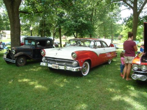 1992 Ford Crown Victoria - A two-tone red and white 1955 Ford Fairlane Crown Victoria is parked on the grass at an outdoor car show.