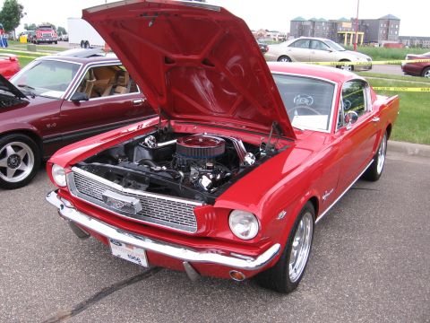 1989 Ford Mustang - A red 1966 Ford Mustang fastback shown hood-up at a car show, revealing a detailed V8 with chrome valve covers and a chrome-lidded round ai…