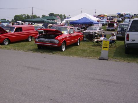 1970 Ford Ranchero - A red pickup truck, likely a 1965 model, is displayed with its hood open at an outdoor car show or event.