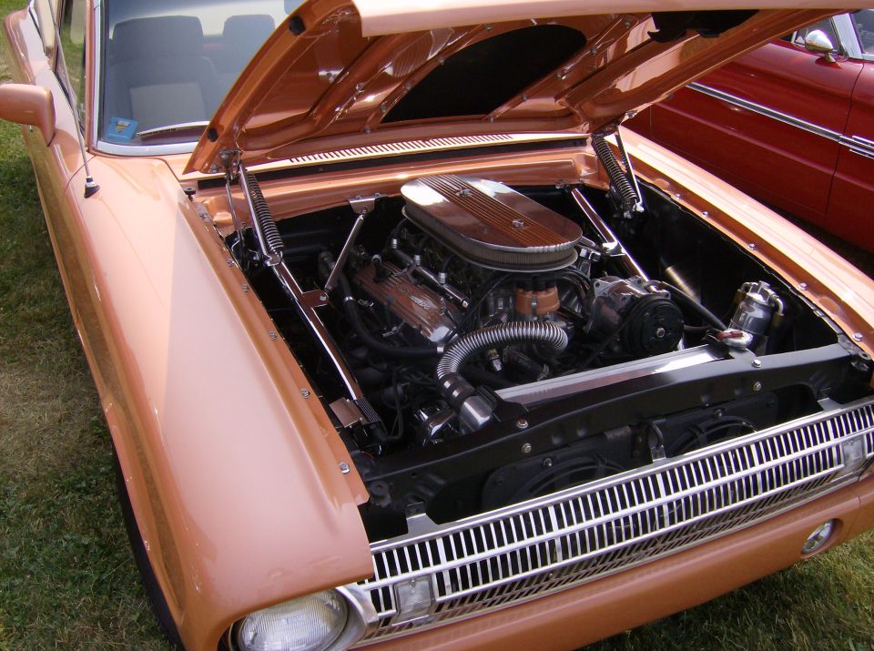 1970 Ford Ranchero with hood open, showing V8 engine and chrome details. Red car visible in background