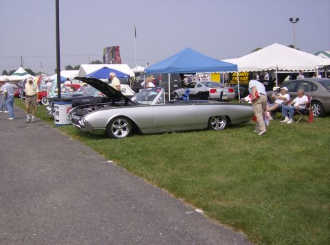 1970 Ford Ranchero - A classic convertible is displayed at an outdoor event with spectators relaxing nearby.