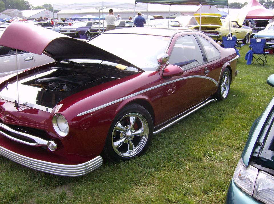 Maroon custom coupe with hood open, chrome trim, and aftermarket wheels parked on grass