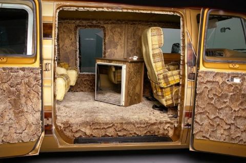 1978 Ford E250 - The interior of a 1978 Ford E250 van features extensive shag carpeting, plaid upholstery, and wood-grain paneling.