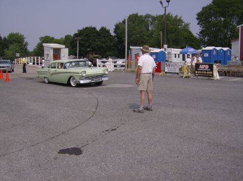 1970 Ford Ranchero - A man stands in a parking lot as a vintage Ford Fairlane sedan drives by.