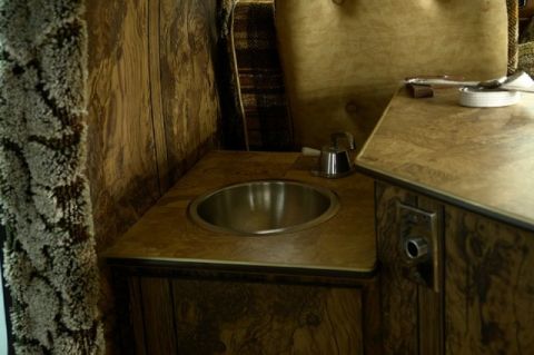 1978 Ford E250 - The interior of a van features a small sink and countertop, with wood paneling and upholstered seating visible.