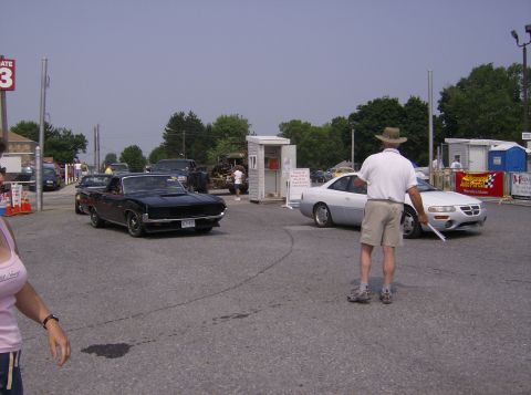 1970 Ford Ranchero - A black convertible is seen from the front in an outdoor lot with other vehicles and people present.