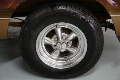 1978 Ford E250 - Close-up of a vehicle's wheel and tire, showing custom chrome rims and wood paneling.