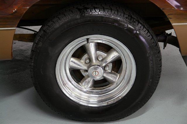 Chrome five-spoke wheel with a black tire on a vehicle with wood paneling