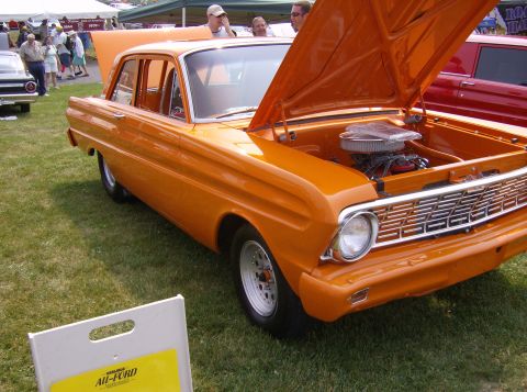 1970 Ford Ranchero - This orange sedan, likely a 1960s model, is displayed with its hood open, revealing the engine and a prominent chrome grille.