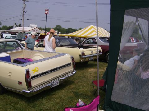 1970 Ford Ranchero - Multiple vehicles are parked on a grassy field under a tent and clear sky.