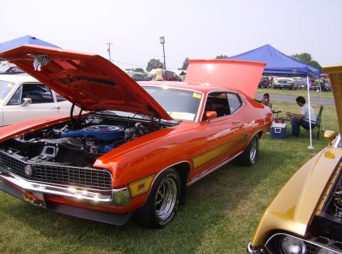 1970 Ford Ranchero - This orange 1970 Ford Ranchero is displayed with its hood open, revealing the engine bay. Another vehicle is partially visible in the foreg…
