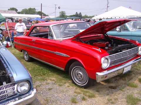 1970 Ford Ranchero - A red 1964 Ford Falcon is displayed with its hood open at an outdoor car show.