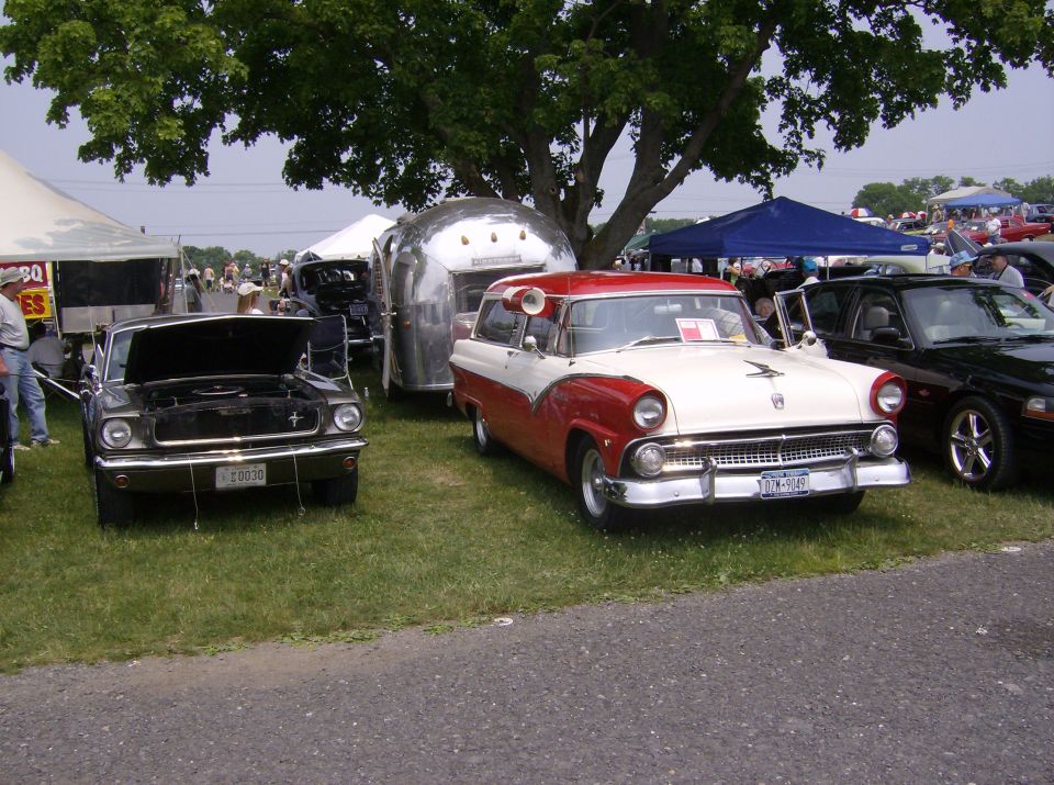 Two-tone red and white 1956 Ford Fairlane Crown Victoria parked next to a Mustang and an Airstream trailer