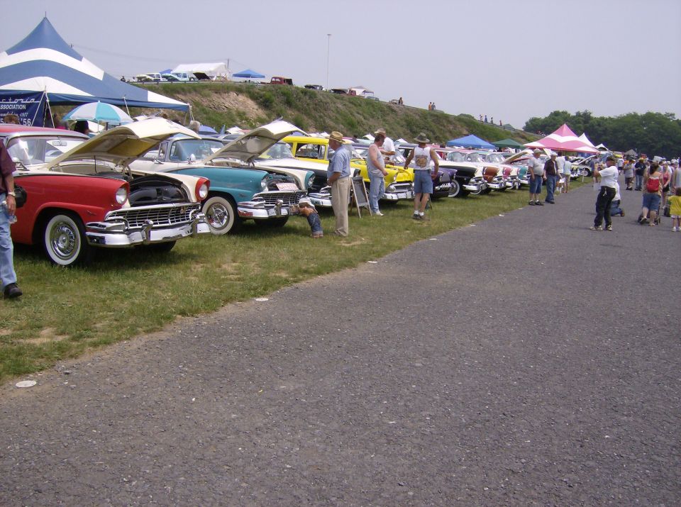Red 1955 Ford Fairlane Crown Victoria with hood open, parked on grass next to other classic cars