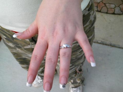 1986 Ford Bronco - A hand displays an engagement ring with a square-cut center stone and a diamond-accented band, complemented by French manicured nails.