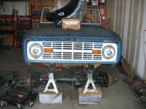 1992 Ford Mustang - The front clip of a blue Ford Bronco is disassembled and supported by jack stands in a garage.