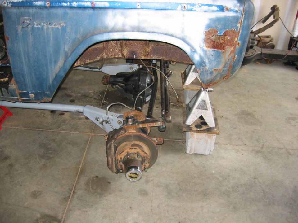 Blue Ford Bronco fender and suspension on jack stands, showing rust and mechanical parts