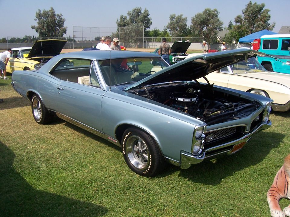 Light blue 1966 Pontiac GTO coupe with hood open, parked on grass at a car show