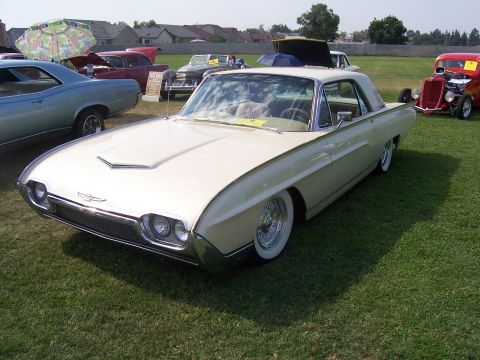 2002 Ford Mustang - A classic Ford Thunderbird is displayed at an outdoor car show with other vehicles in the background.
