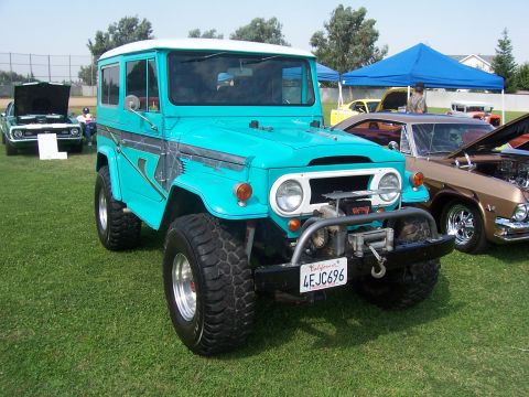 2002 Ford Mustang - A turquoise off-road vehicle with a white roof and a winch is parked on a grassy field next to other vehicles.
