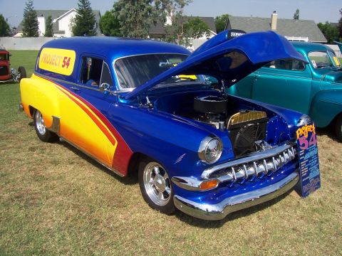 2002 Ford Mustang - A custom blue and yellow sedan delivery, identified as "Project 54", is displayed with its hood open at an outdoor event.