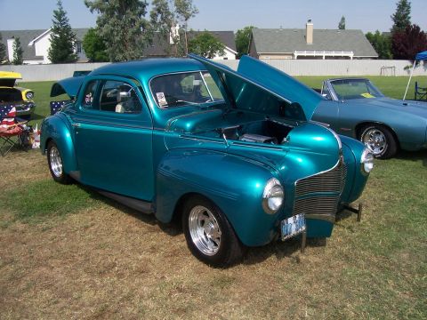2002 Ford Mustang - A teal coupe is displayed with its hood open, revealing the engine compartment. A second vehicle is visible in the background.